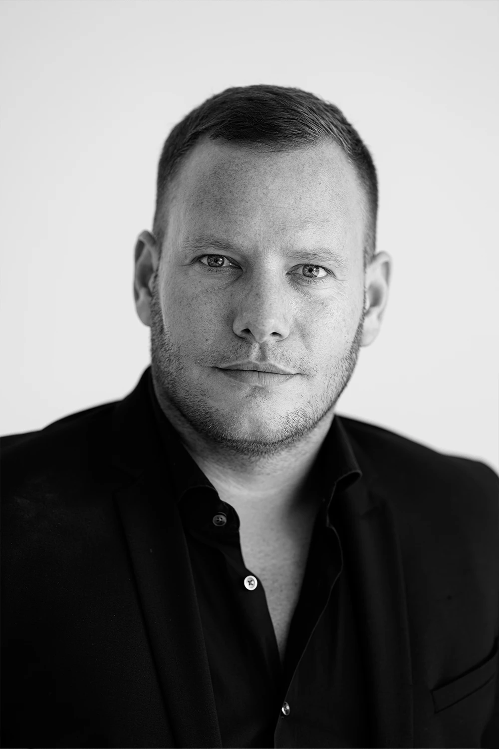 Ein Schwarz-Weiß-Foto zeigt einen lächelnden Zahnarzt vor einem hellen neutralen Hintergrund. Er trägt ein dunkles Hemd. Der abgebildete Arzt ist Oliver Spitz, der Gründer von ELEVEN ELEVEN.